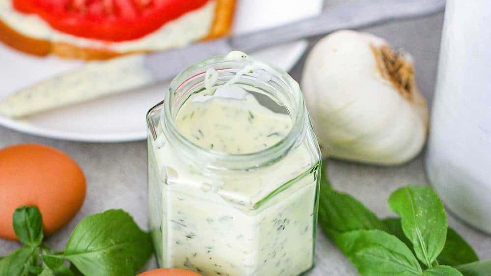 A small jar containing homemade garlic basil aioli next to an egg and garlic. 
