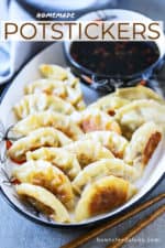 A platter of potstickers next to a bowl of dipping sauce.