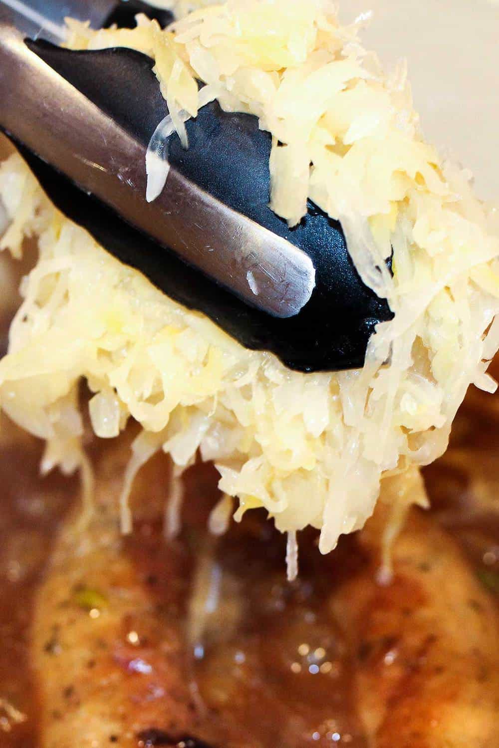 Sauerkraut being lowered into a pot of ale-braised bratwurst