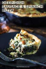 A slice of deep-dish pizza with sausage and spinach with a bite taken out of it sitting on a blue plate with a fork next to it.