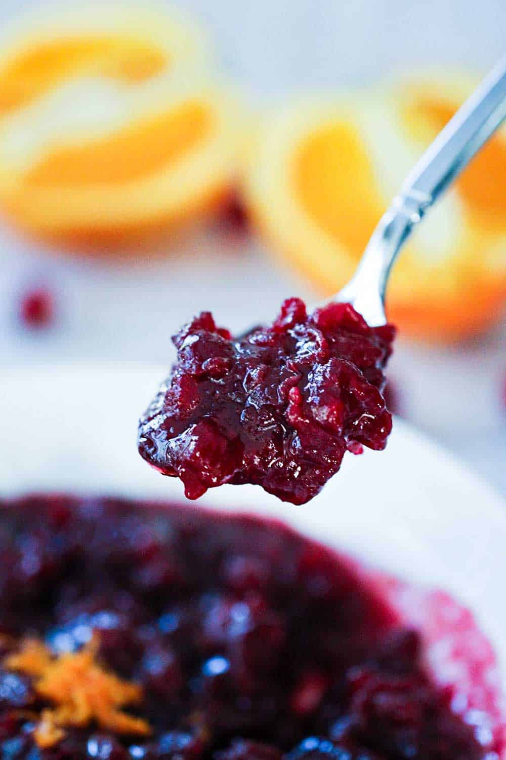 A spoon holding homemade cranberry sauce of a bowl of cranberry sauce. 