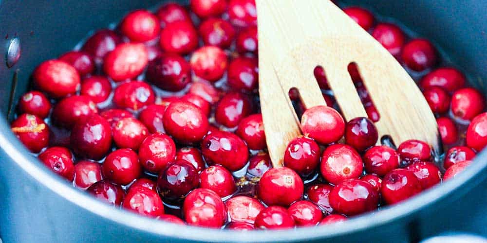 A pan holding fresh cranberries with a wooden spoon in it. 