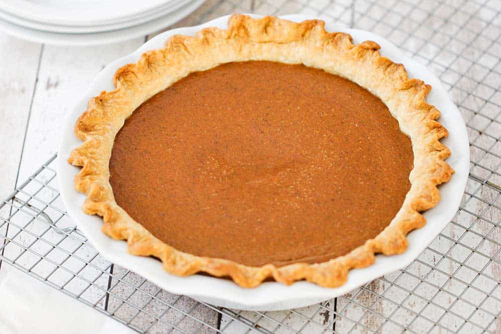 A fully cooked classic pumpkin pie in a white pie dish sitting on a baking rack. 