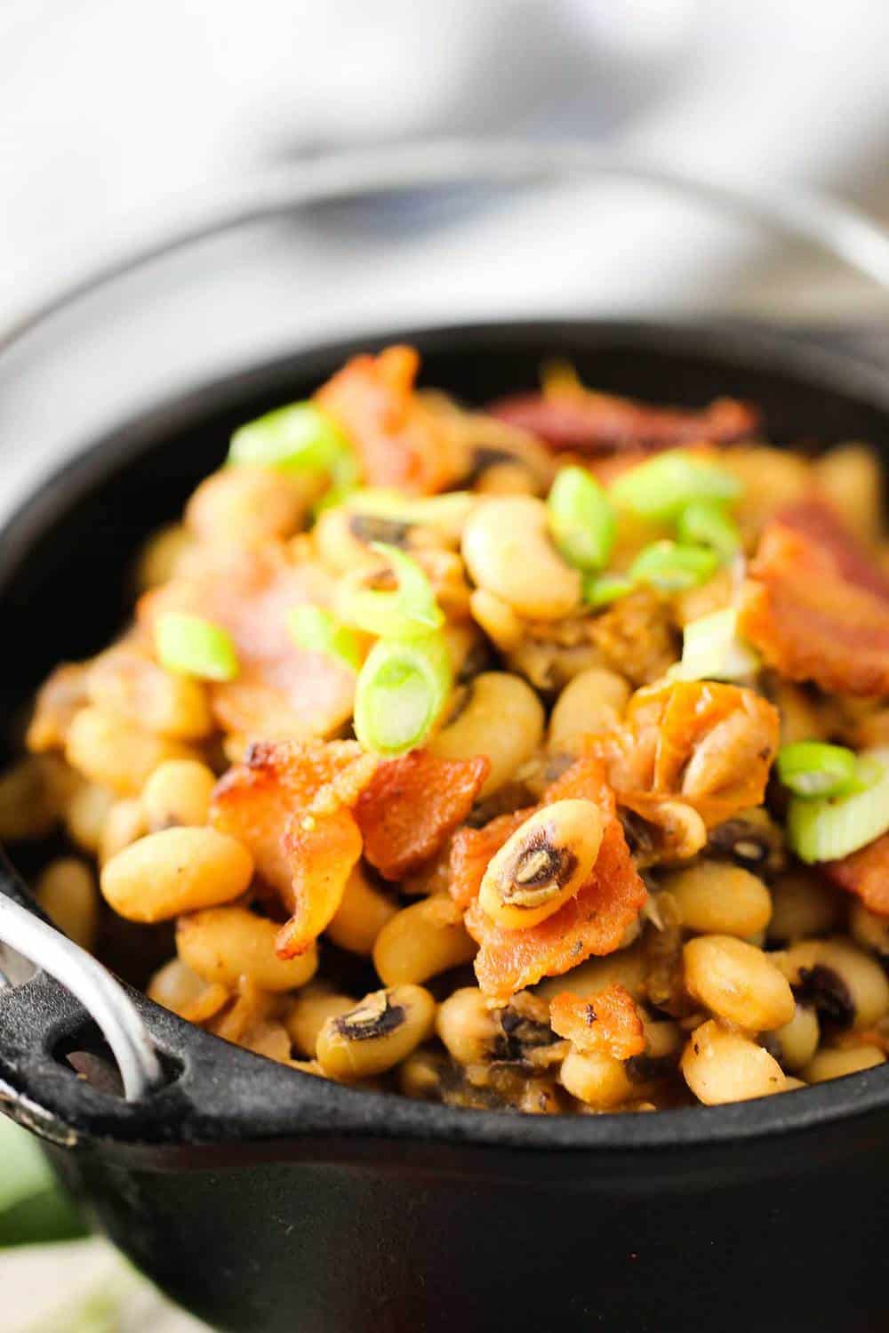 A black crock full of black-eyed peas with tomatoes