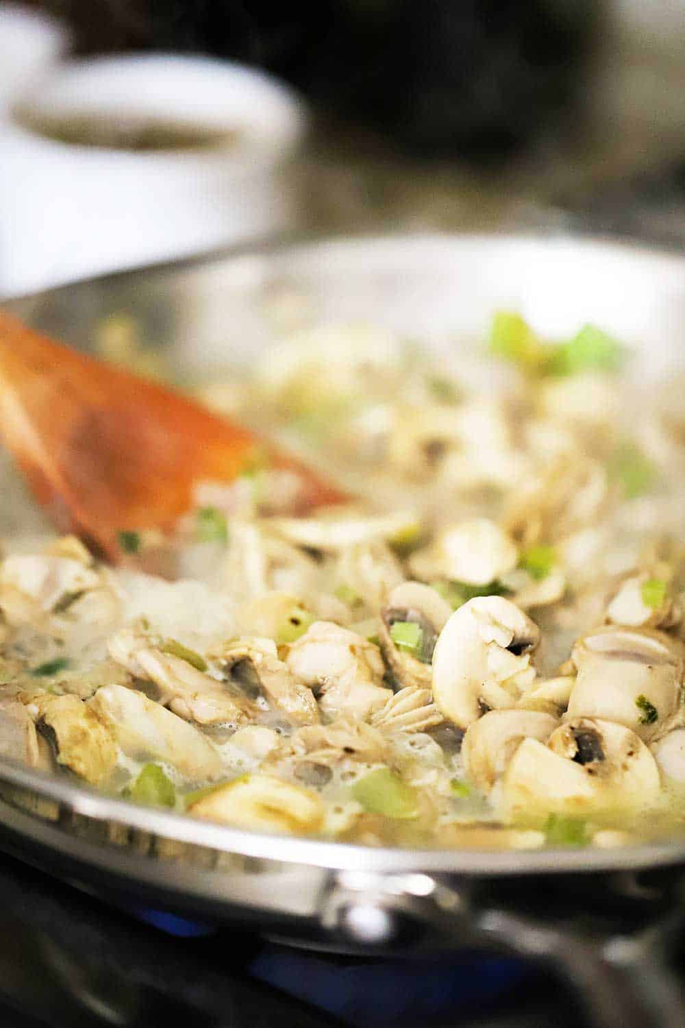 A large silver skillet filled with oysters and mushrooms and liquid that has been released from them. 