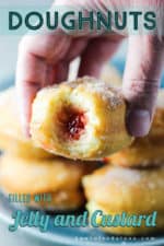 A hand holding a jelly and custard doughnut with a bite taken out of it.