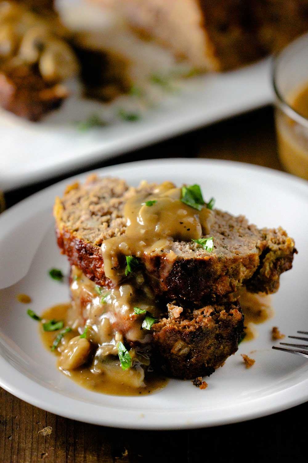 Two slices of meatloaf on a white plate with mushroom gravy poured over the top. 