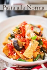 A white dinner bowl filled with a pile of Pasta alla Norma topped with crumbled cheese.
