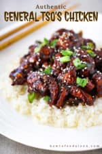 A white plate of General Tso's Chicken on a bed of white rice with a pair of chop sticks nearby.