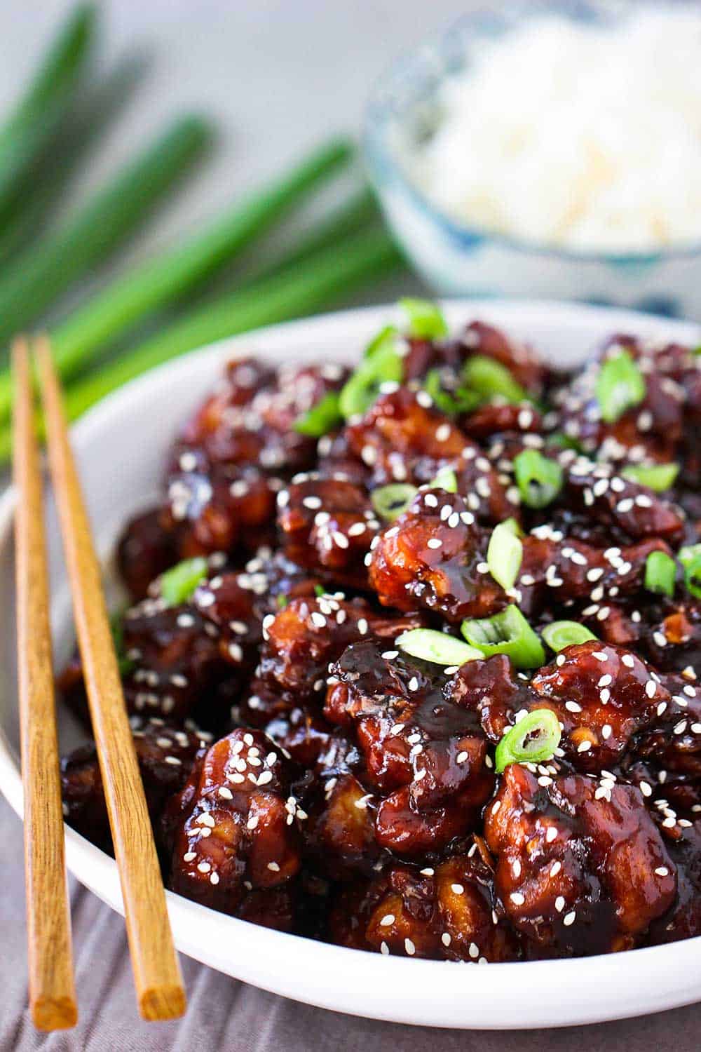 A close-up view of a white bowl holding prepared General Tso's Chicken next to another bowl of white rice. 