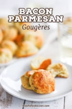 A small white dessert plate holding two parmesan bacon gourgeres next to a plate full of them.