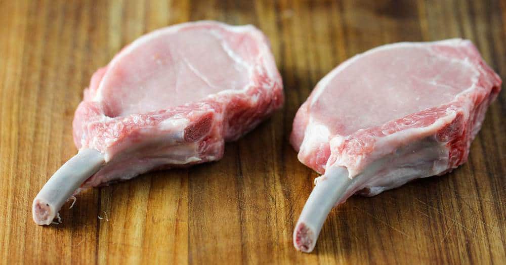 Two center-cut bone in pork chops on a cutting board.