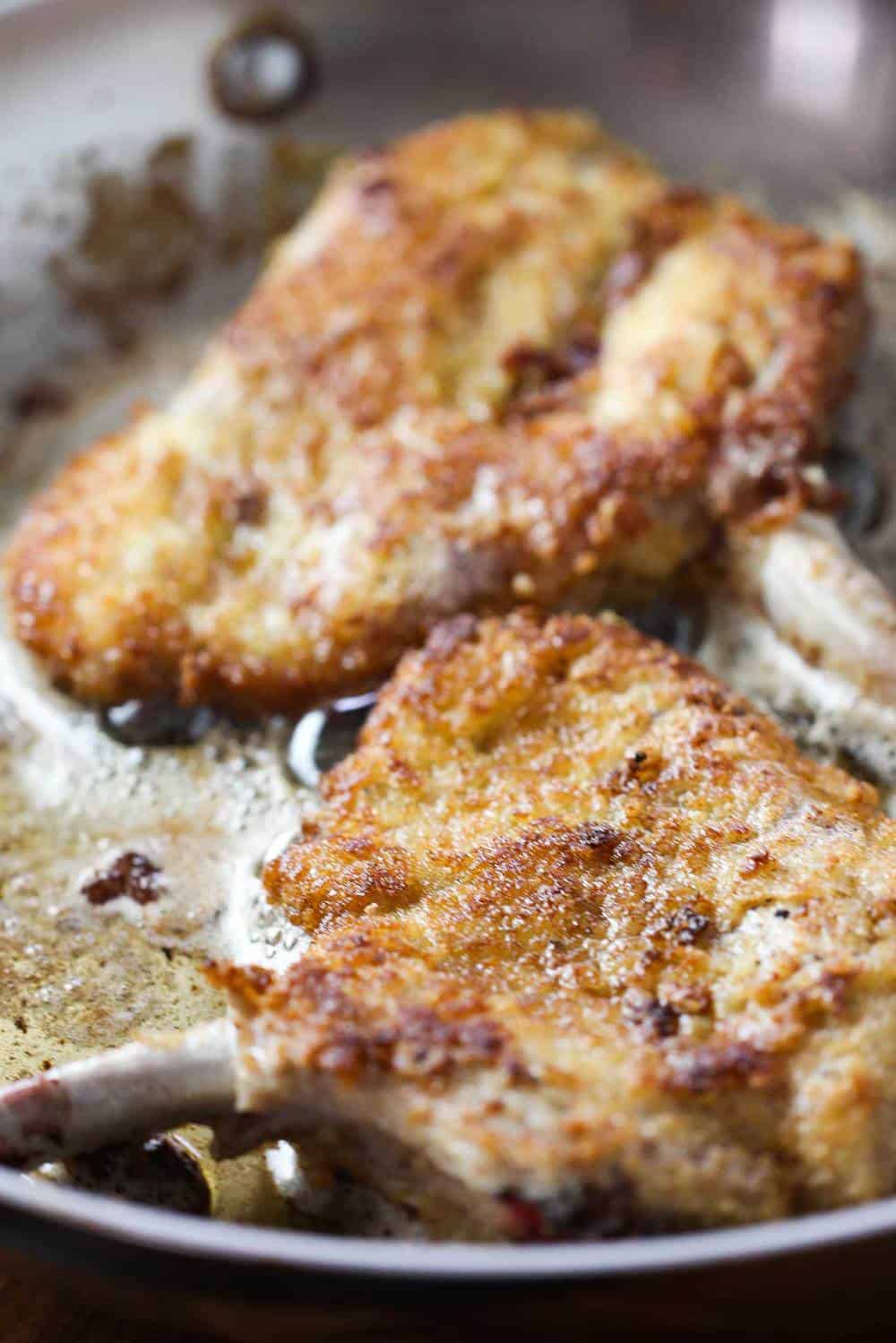 Breaded pork chops cooking in a large metal skillet. 