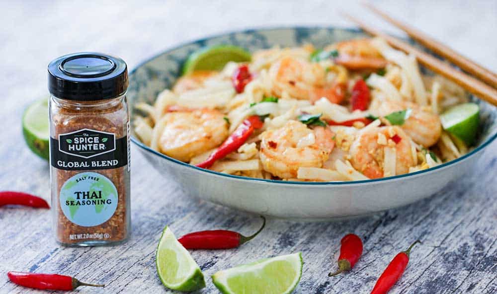 A bowl of authentic shrimp pad Thai with a bottle of Thai seasoning next to it. 