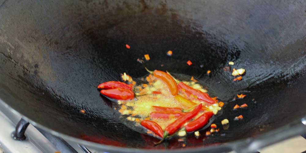 Thai peppers and garlic being stir-fried in a black wok. 