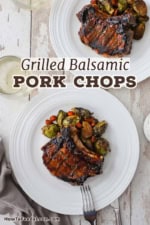 An overhead view of two white dinner plates filled with serving of grilled balsamic glazed pork chops with roasted Brussels sprouts and carrots.