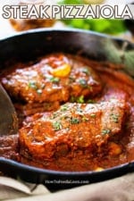 A cast-iron skillet filled with to seared steaks covered in a tomato sauce for steak pizzaiola.