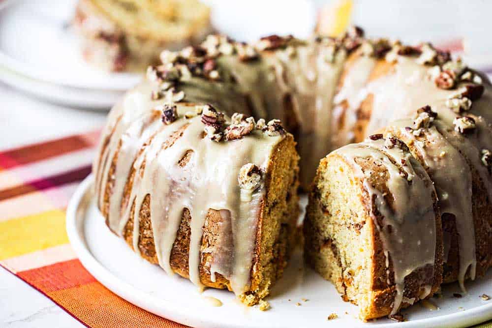 A sweet potato bundt cake on a white circular plate with a slice missing. 