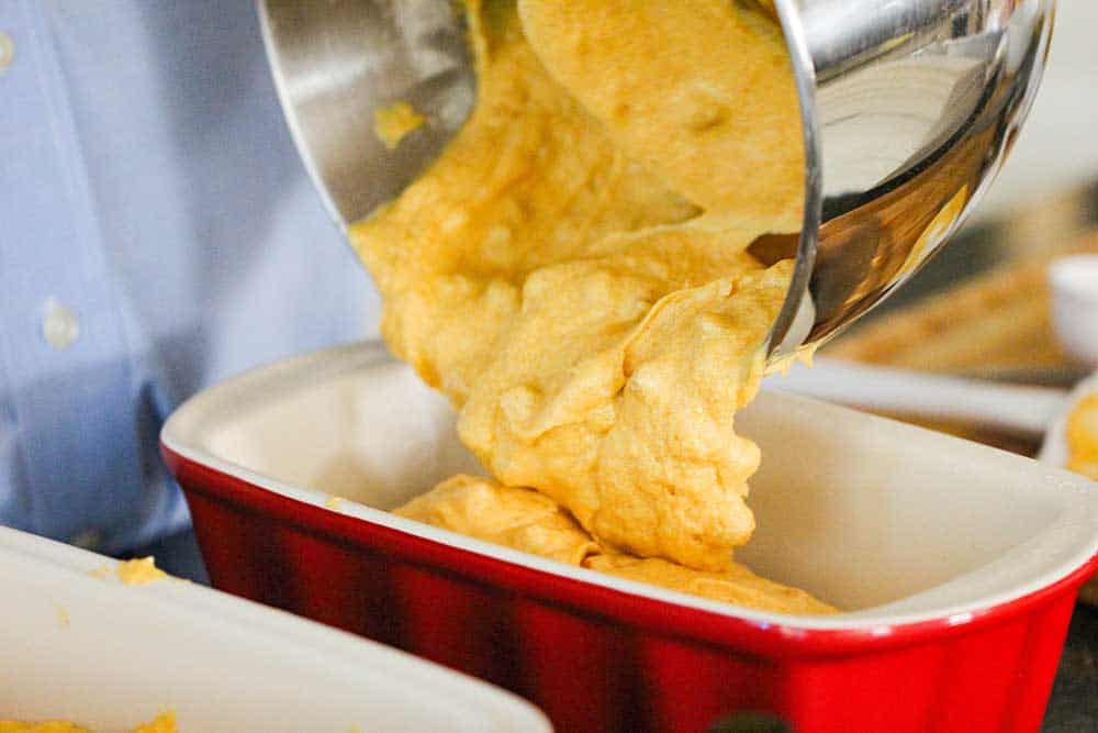 Pumpkin butterscotch batter being poured from a large silver bowl into ceramic loaf pans. 