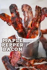 Five strips of maple pepper bacon sitting upright in a small silver pale with extra strips of bacon laying around the base of the pale.
