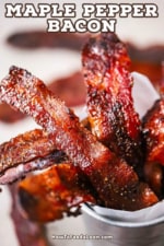 A close-up view of cooked strips of crispy maple pepper bacon sitting in a small silver pale lined with white butcher paper.