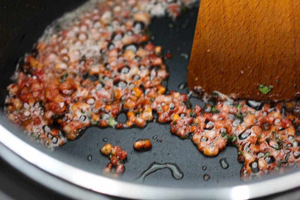 Cubed pancetta and chopped fresh sage being sautéed in the base of a pot. 