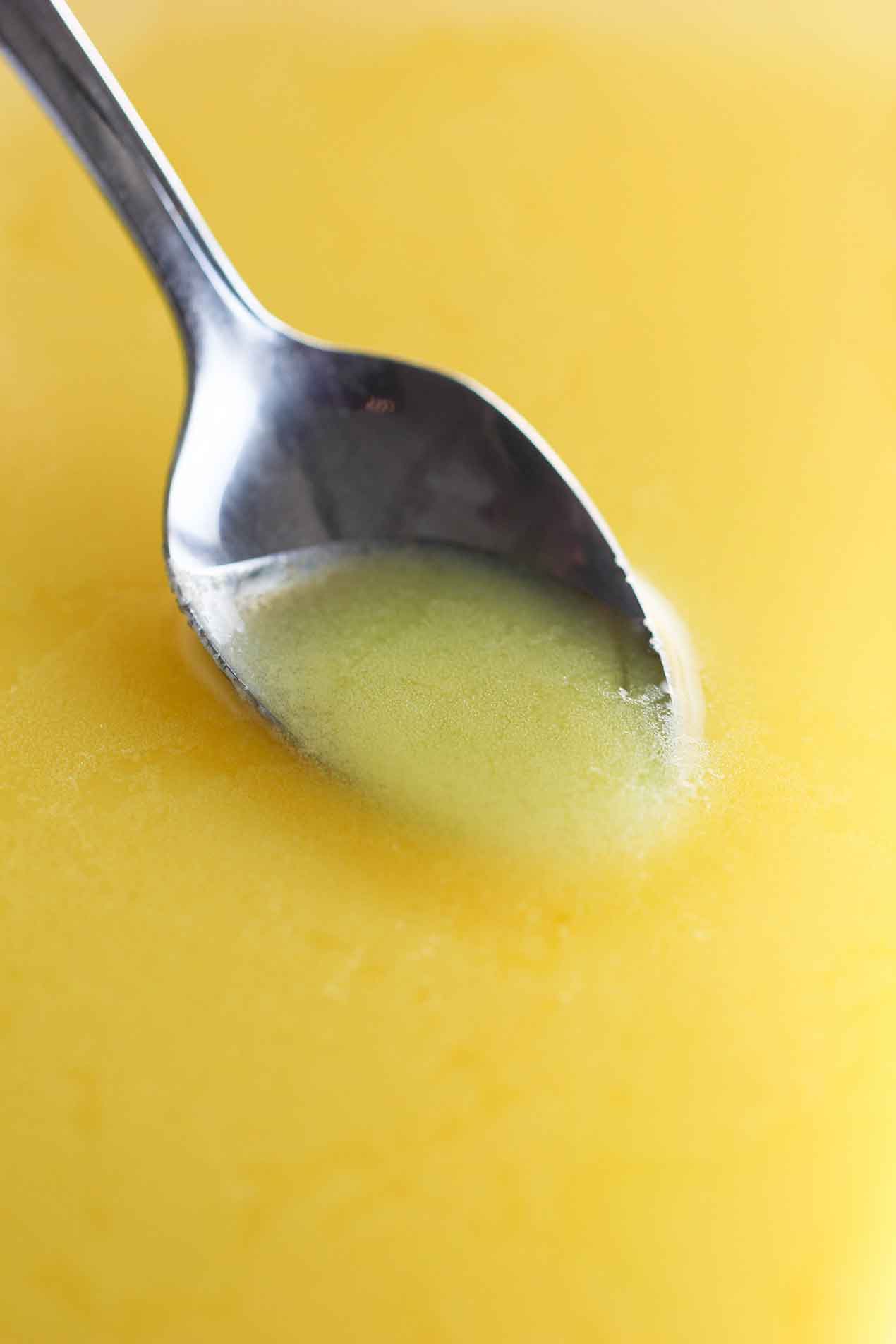 A spoon being used to scrape congealed chicken fat from the top of a stock pot filled with chilled chicken broth