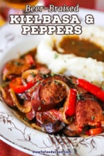 A close-up view of an antique bowl filled with a helping of beer-braised kielbasa and peppers next to a pile of mashed potatoes and gravy.