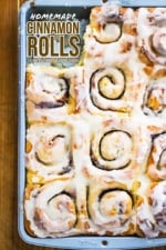 A metal baking pan filled with homemade cinnamon rolls with a roll missing from the lower left-hand corner.