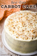 An overhead view of a three layered carrot cake topped with with cream cheese icing and toasted coconut flakes.