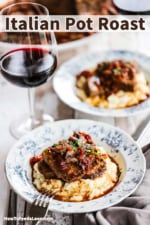 Two antique dinner bowls filled with mashed potatoes and topped with slices of Italian pot roast all sitting next to a glass of red wine.