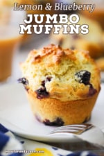 A close-up view of a lemon and blueberry jumbo muffin sitting a small white plate with a fork next to it.