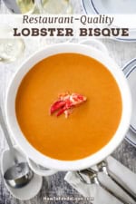 An overhead view of a large white soup terrine filled with lobster bisque with a meat from a lobster claw resting in the middle of the soup.