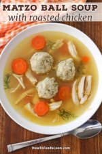 An overhead view of a shallow white soup bowl filled with homemade matzo ball soup with chicken and carrots and several sprigs of fresh dill.