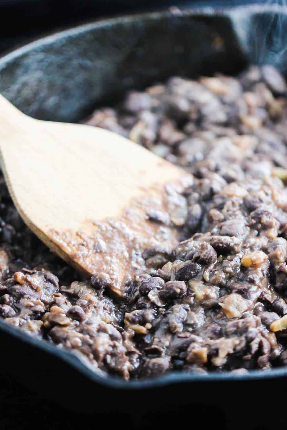 A close-up view of black beans that have been sautéd with onion in pork lard and then lightly mashed in a saucepan
