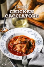 A straight-on view of a vintage individual bowl filled with a helping of chicken cacciatore and sitting next to a stemless glass of white wine.