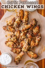 An overhead view of a serving of garlic Parmesan wings on two pieces of brown paper with two small jars of blue cheese dressing nearby.