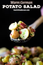 A person holding up a wooden spoon that is filled with a small pile of German potato salad over a bowl of the same.