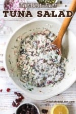 An overhead view of a ceramic bowl filled with homemade tuna salad with a wooden inserted in the side of the salad.