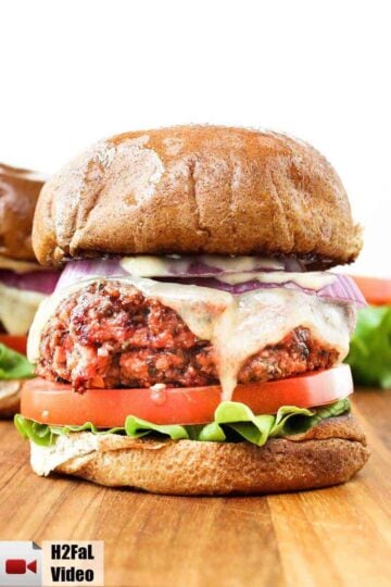 A veggie burger with melting cheese on a wooden board.