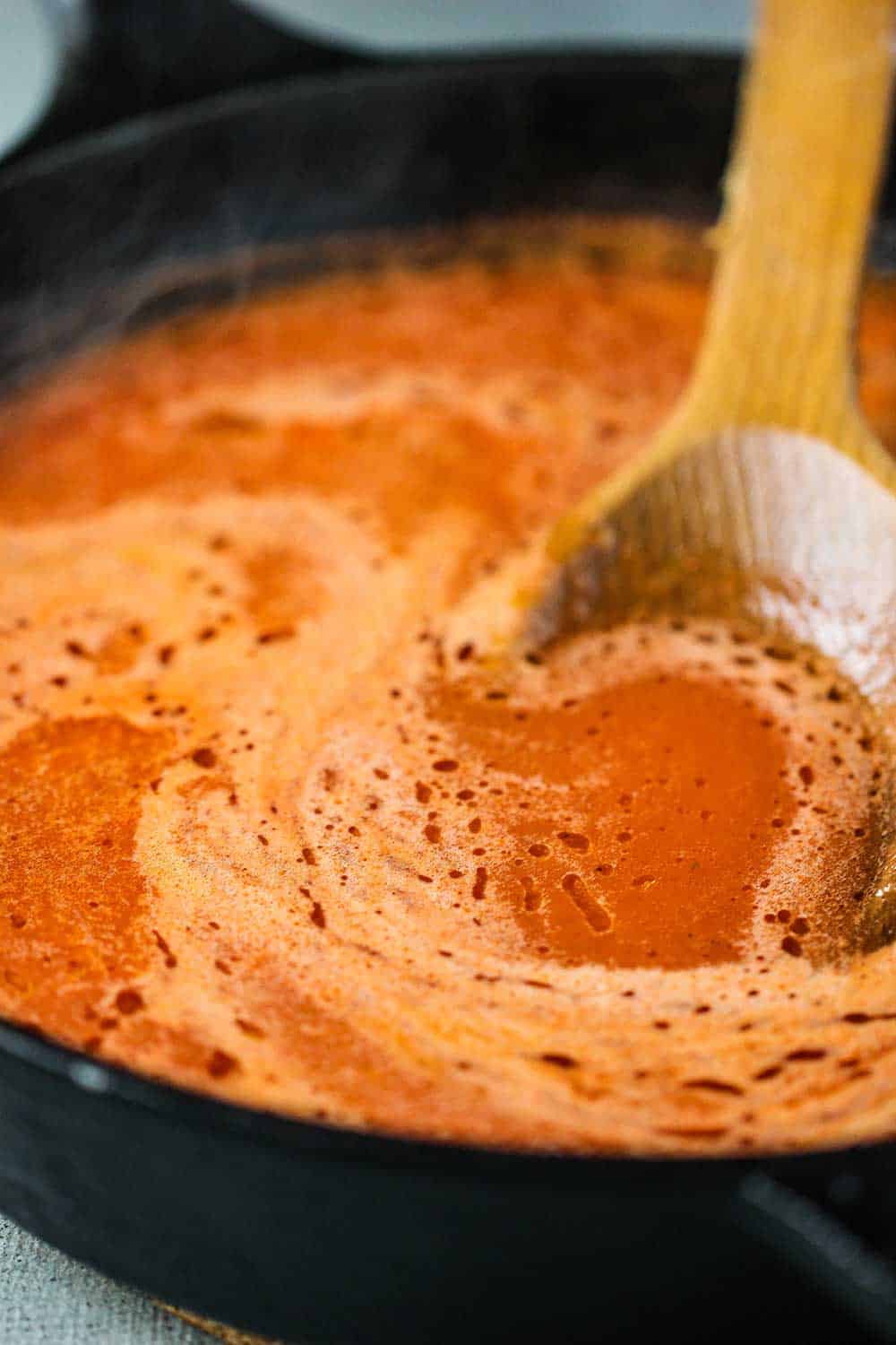 Red sauce in a cast iron skillet with a wooden spoon for Chile rellenos. 