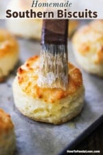 A pastry brush being used to smear melted butter over the top of a Southern biscuit on parchment paper.