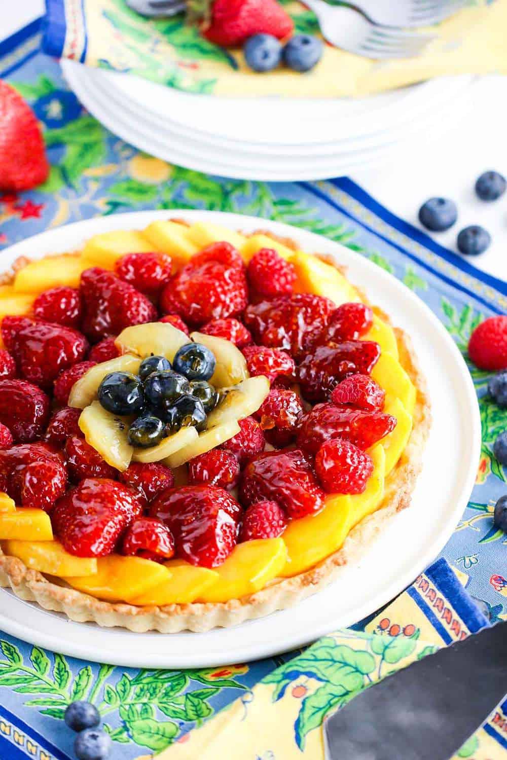 An overhead view of a summer fruit tart that is sitting on a circular white serving plate.