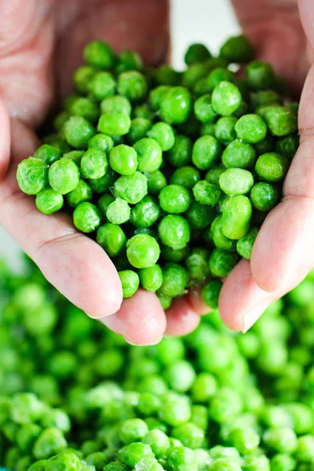 Hands holding frozen peas that have been cooked