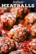 A close-up view of Italian meatballs in a marinara sauce topped with shaved parmesan and chopped parsley.