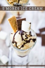 An ice cream parlor glass holder filled with s'mores ice cream topped with a piece of graham cracker, a piece of chocolate and a toasted marshmallow.