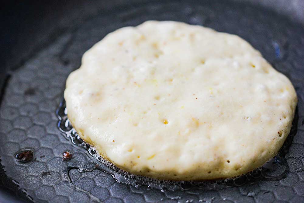 A circular shape of pancake batter on a hot skillet. 