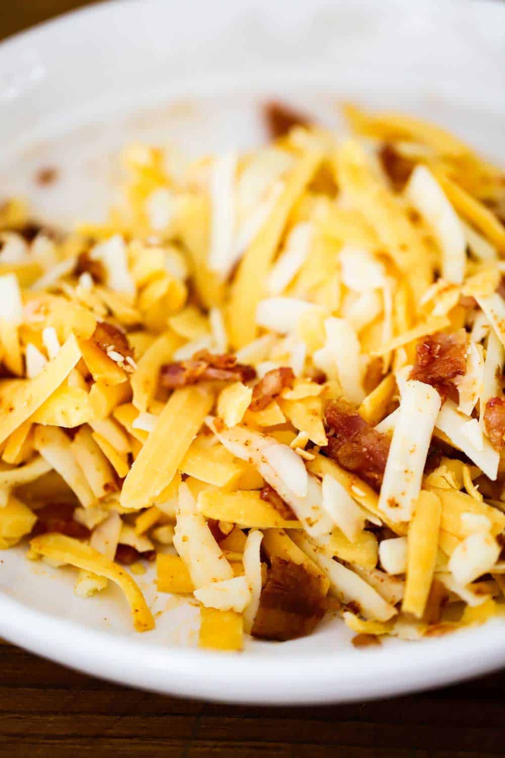 A white bowl filled with shredded cheddar and Monterey Jack cheese and crumbled bacon. 