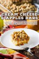 A cream cheese and apples bar sitting on a white dessert plate in front of a baking dish filled with the full dessert.