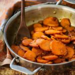 A large silver skillet filled with cooked candied yams and wooden spoon.